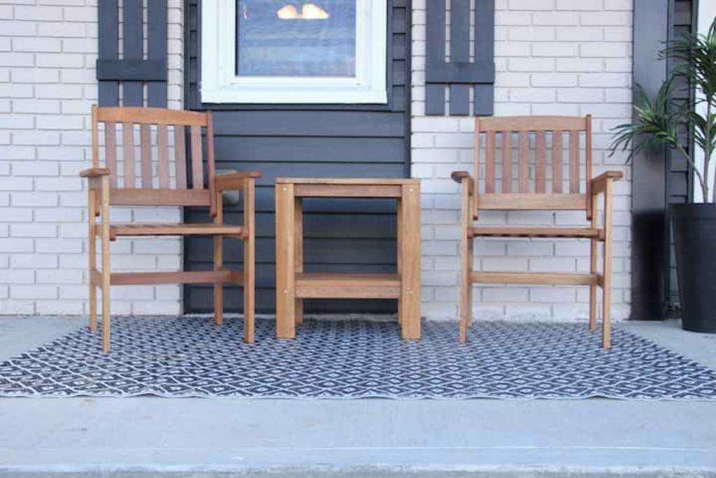A wooden bench and table set against a white brick wall with a framed picture above.