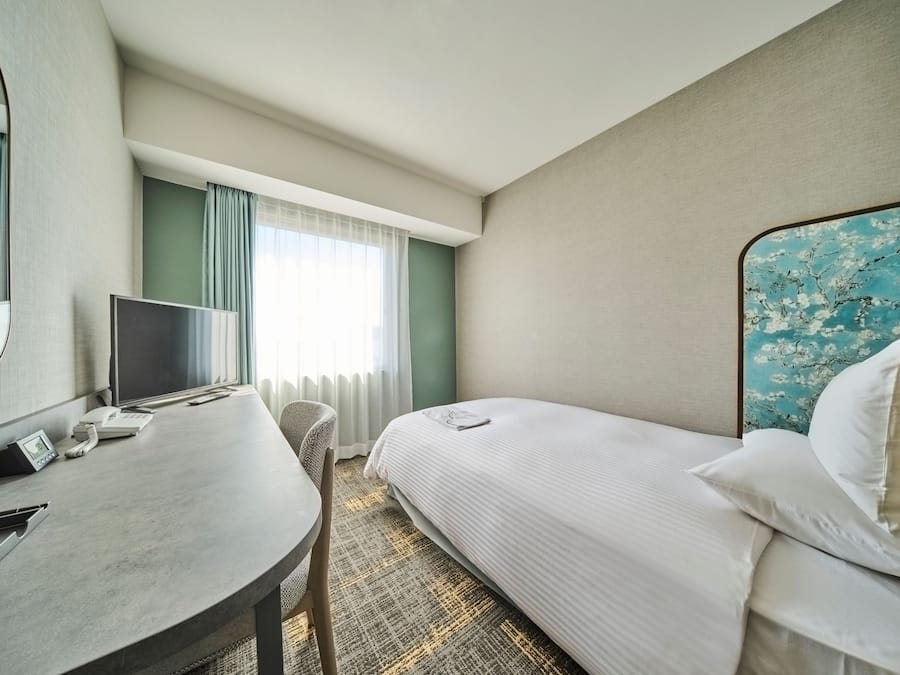 Una habitación de hotel con una cama, un escritorio, un televisor y una ventana con cortinas.