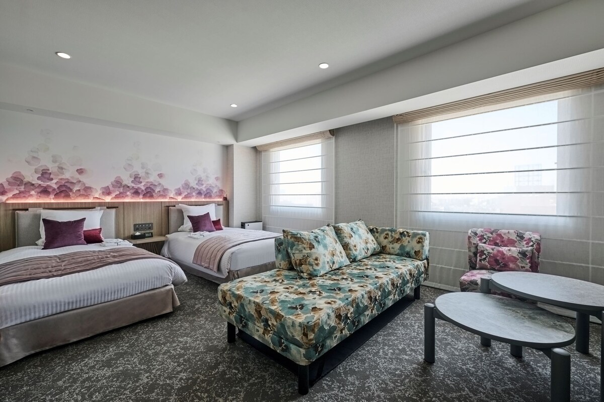 A hotel room with two beds, a sofa, a small table, and a decorative wall.