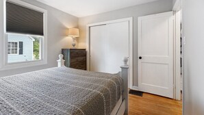 Un dormitorio con una cama, una mesita de noche, una lámpara, un aparador y una puerta.