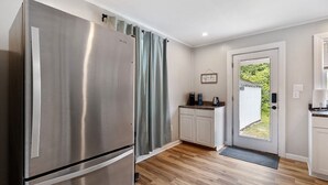 Cocina compacta con refrigerador de acero inoxidable, una pequeña encimera con cafetera y una puerta que da a un jardín.
