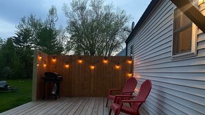 Una terraza de madera con una parrilla y dos sillas rojas.