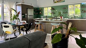 Moderni keittiö, jossa on keskeinen saareke, ruokailutila tuoleineen ja suuri ikkuna, josta tulee runsaasti luonnonvaloa.