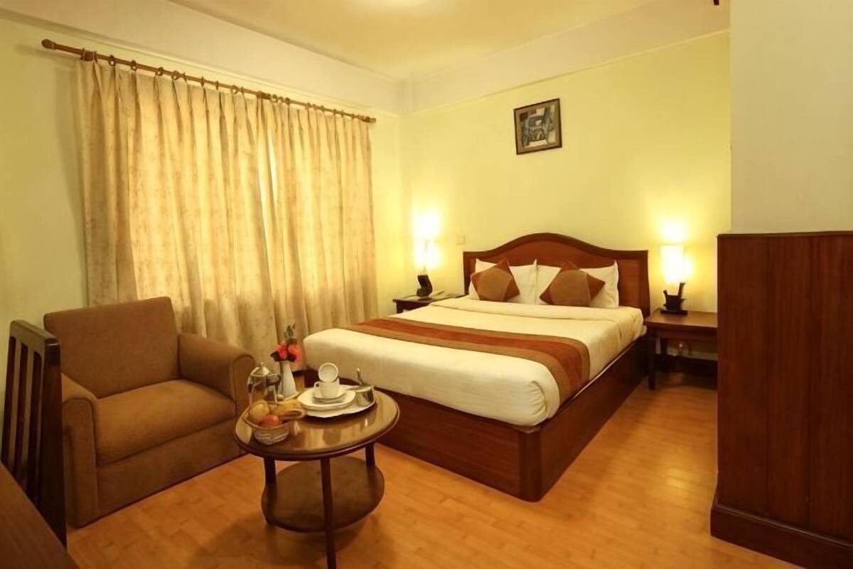 Une chambre d’hôtel avec un lit, une chaise, une petite table avec un plateau, et un rideau.