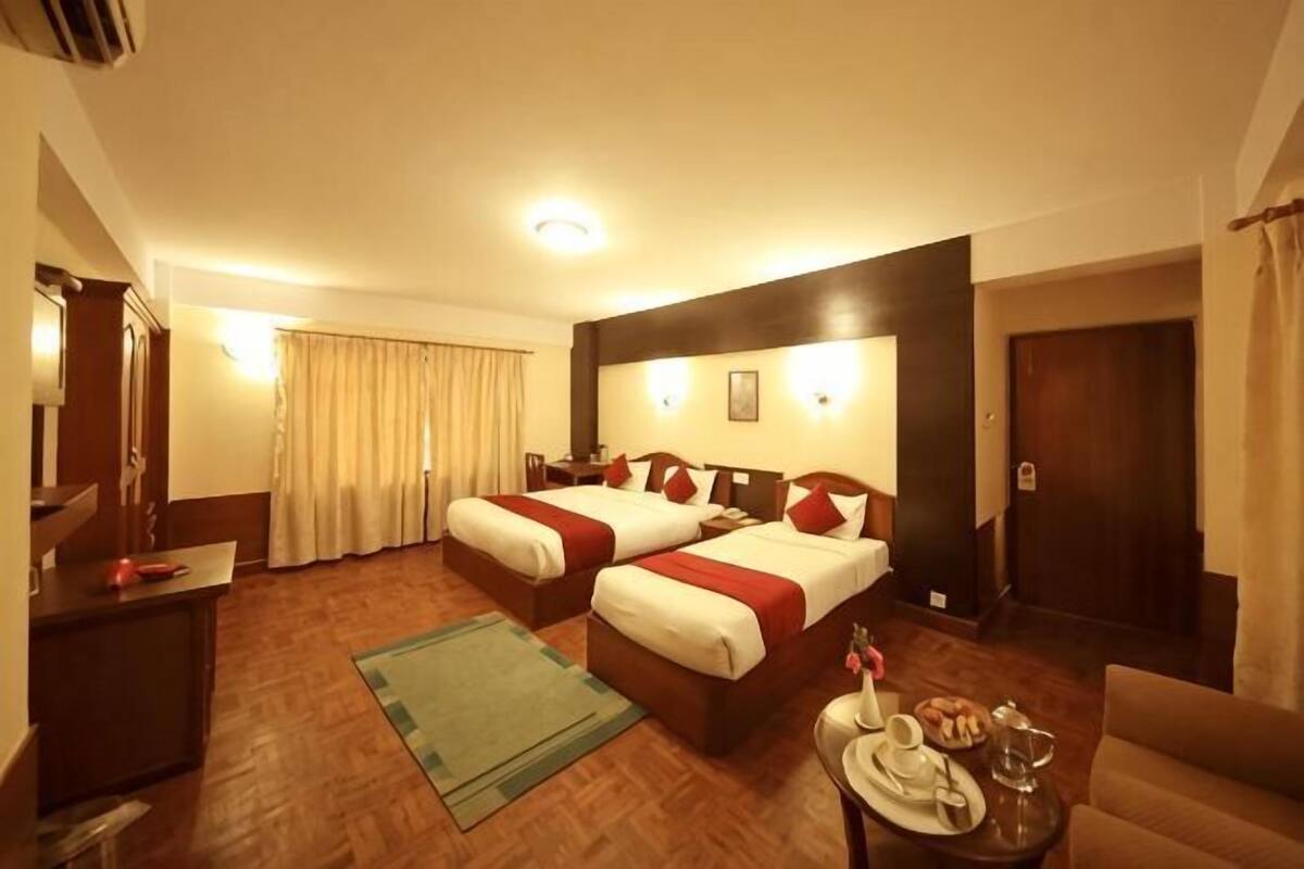 Une chambre d’hôtel avec deux lits, un bureau, une chaise, une petite table avec un plateau, et un canapé.