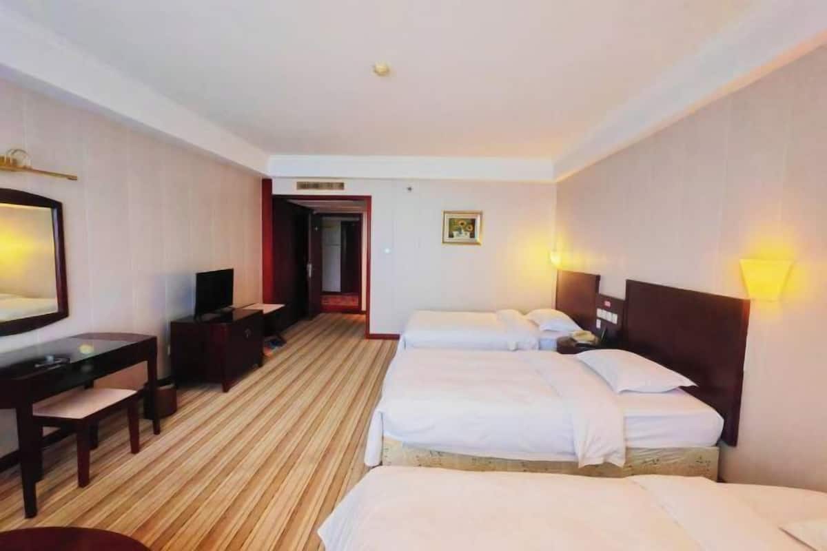 A hotel room with two beds, a desk, a television, and a mirror.