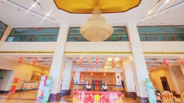 Eine Hotelhalle mit einem großen Chandelier, einer Rezeption und einer hohen Decke mit Verzierungen.