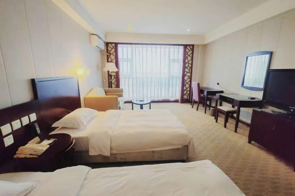 A hotel room with a bed, a desk, a TV, and a window with curtains.