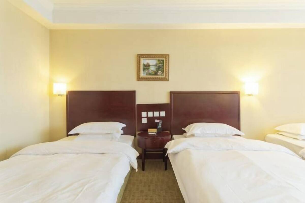 A hotel room with two beds, a small table, a nightstand, and a framed picture on the wall.