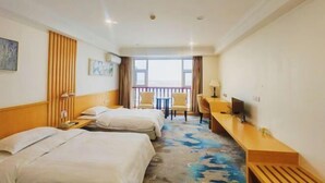 Ein Hotelzimmer mit zwei Betten, einem Schreibtisch, einem Stuhl, einem Fernseher und einem Balkon mit Blick.