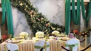 Ein festlich gedeckter Esstisch vor einer Marmorwand, mit grünen Vorhängen und floralen Dekorationen.