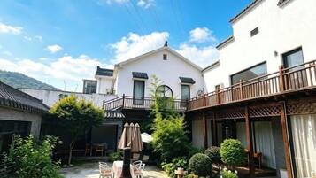 A courtyard with a white building, wooden balcony, and outdoor seating.