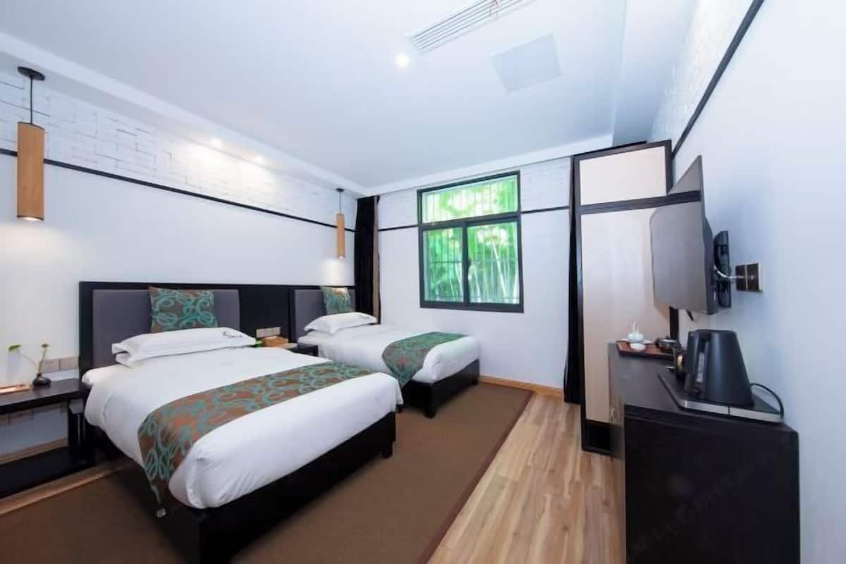 A hotel room with two beds, a TV, a desk with a coffee maker, and a window with a view of trees.