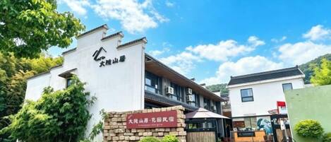 A hotel entrance with a sign, a pathway, and a building with a traditional architectural style.