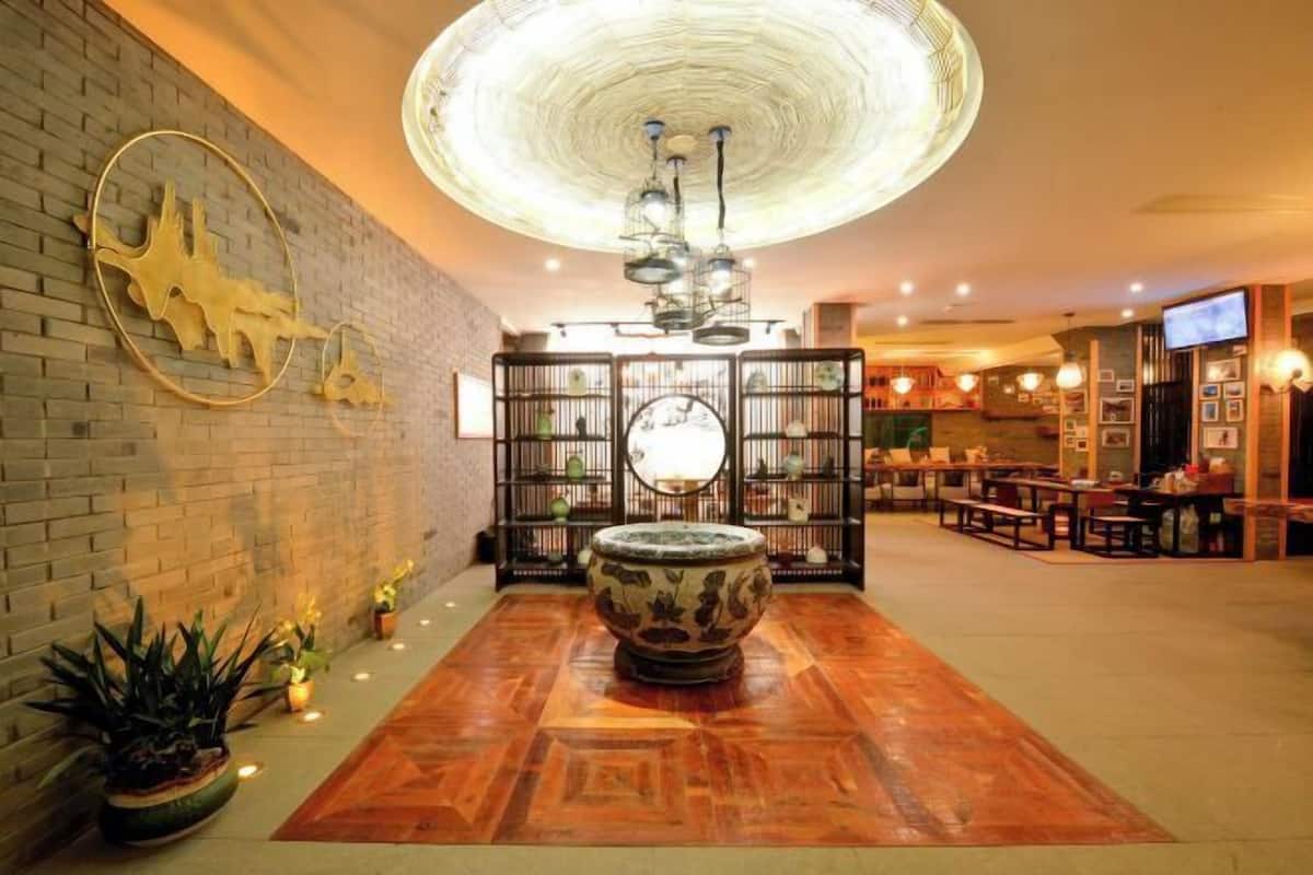 A lobby with a central decorative bowl, a brick wall with a sculpture, a ceiling light fixture, and a seating area with tables and chairs.