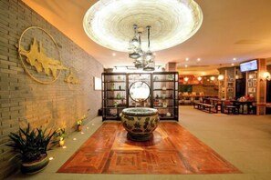 A lobby with a central decorative bowl, a brick wall with a sculpture, a ceiling light fixture, and a seating area with tables and chairs. - Wuxi Dayin Mountain Residence Garden Homestay (Wuxi)