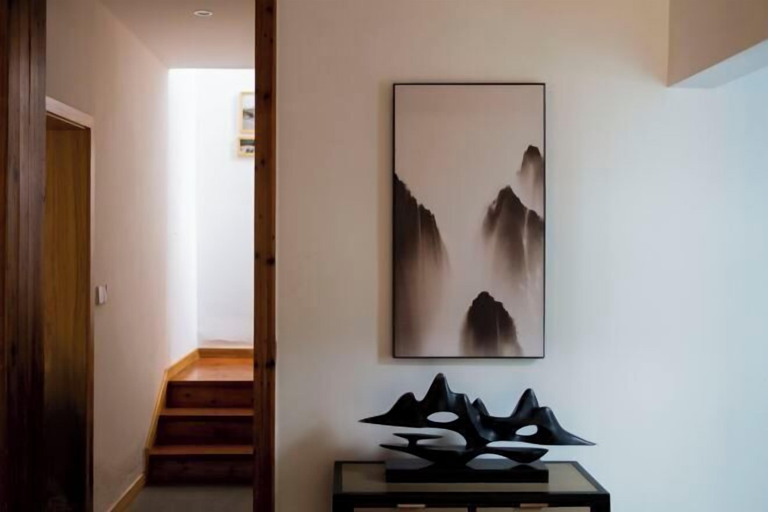 Un pasillo con una escalera, un cuadro abstracto enmarco y una escultura geométrica negra sobre una consola.