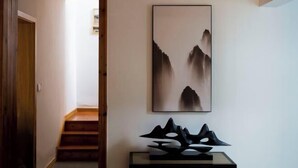 A hallway with a staircase, a framed abstract painting, and a black geometric sculpture on a console table. - Wuxi Dayin Mountain Residence Garden Homestay (Wuxi)