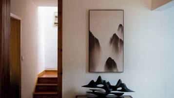 Un pasillo con una escalera, un cuadro abstracto enmarco y una escultura geométrica negra sobre una consola.