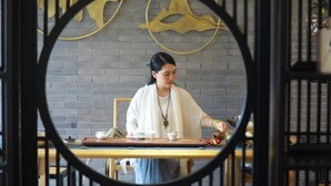 A person sitting at a table with a tea set, in a room with a brick wall and decorative golden elements. - Wuxi Dayin Mountain Residence Garden Homestay (Wuxi)