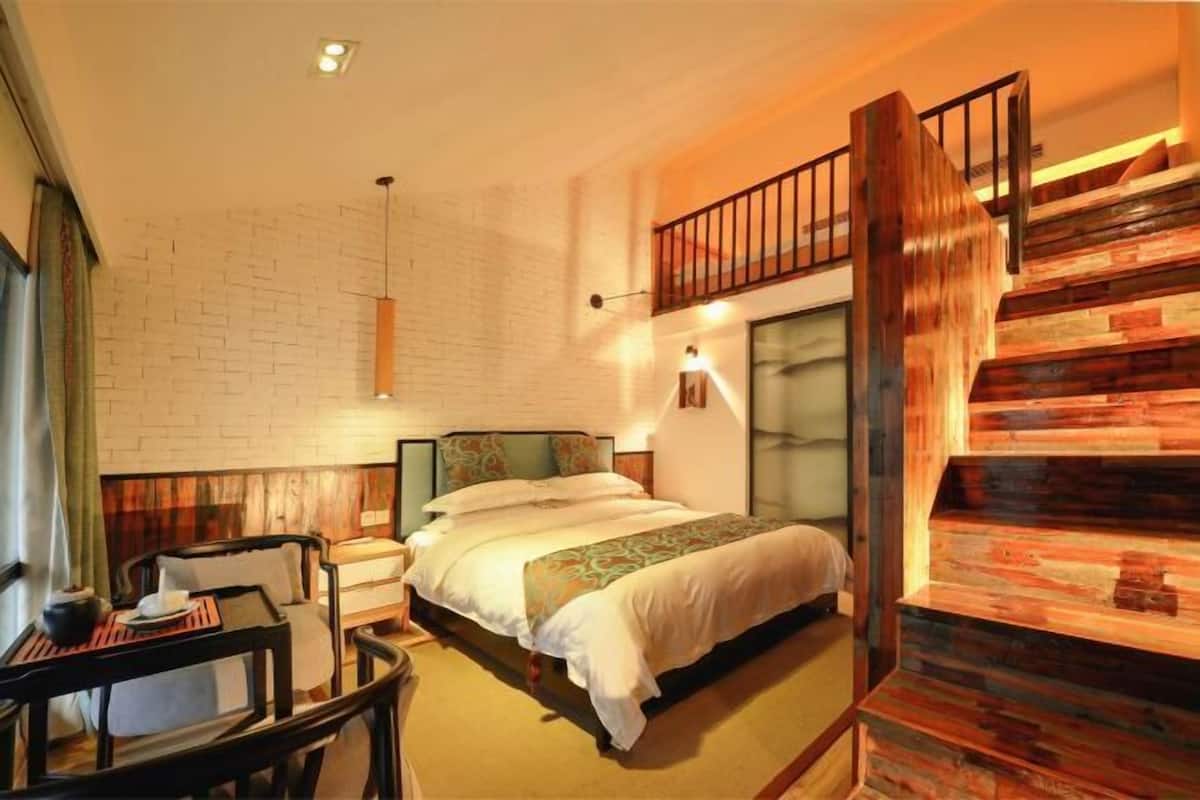 A bedroom with a bed, bedside tables, a chair, a wooden staircase, and a brick wall.