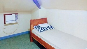 Una cama individual con estructura de madera y un cojín estampado, un equipo de aire acondicionado instalado en la pared y un piso cubierto de moqueta verde.