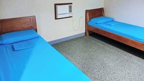 Una habitación con dos camas individuales, un equipo de aire acondicionado pequeño en la pared y una alfombra estampada.