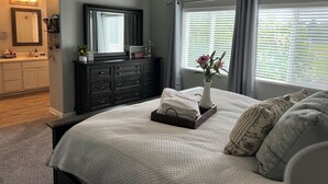 A bedroom with a large bed, a dresser, a vanity, and a window with blinds. - 4 Bedroom with all the things! (Eugene)