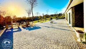 Une cour dallée, agrémentée de bancs en pierre et de jardinières, un ciel dégagé et un bâtiment à la façade moderne.