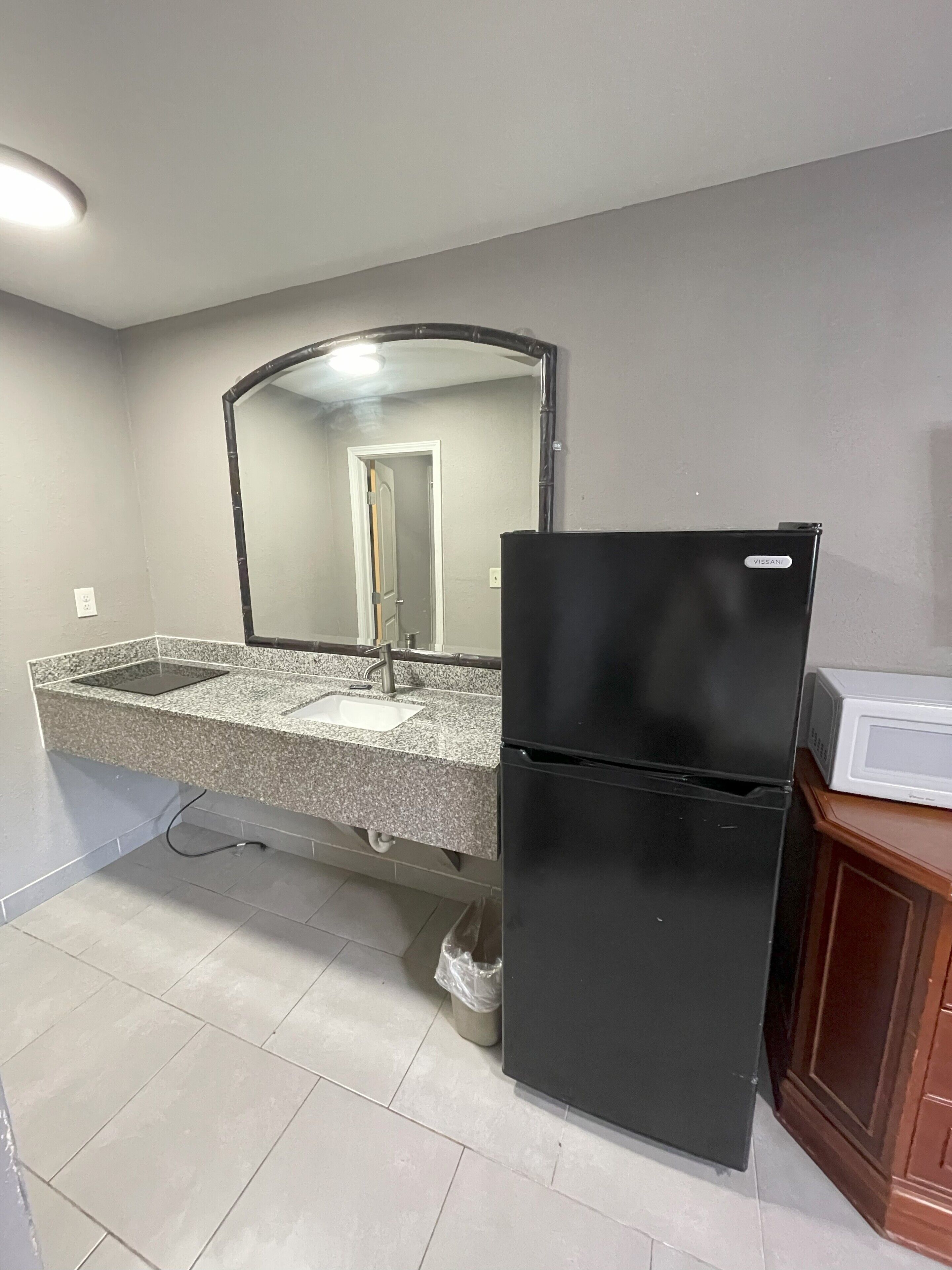 Una cocina con encimera de granito, refrigerador negro y microondas sobre un mueble de madera.