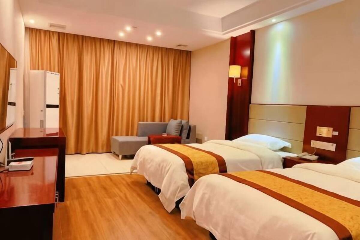 A hotel room with two beds, a desk, a chair, and a large window with curtains.