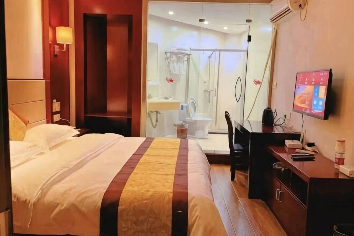 A hotel room with a bed, a desk, a television, and a shower area.