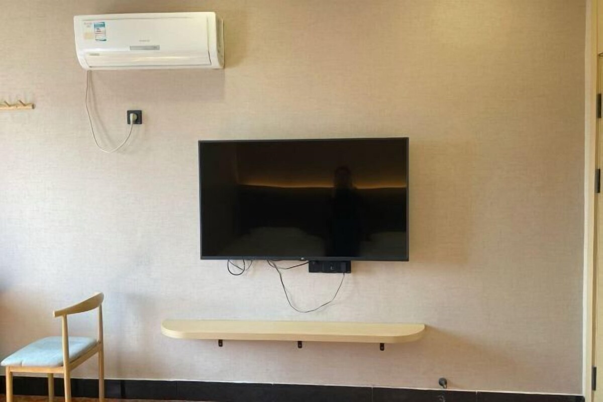 A room with a mounted flat-screen TV, a wall-mounted air conditioner, and a small shelf below the TV.