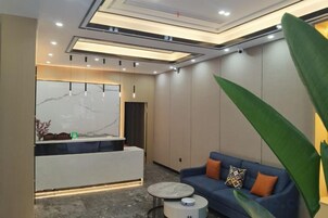 Uma área de recepção moderna com balcão de mármore, um sofá azul com almofadas laranja e uma mesa de centro redonda.