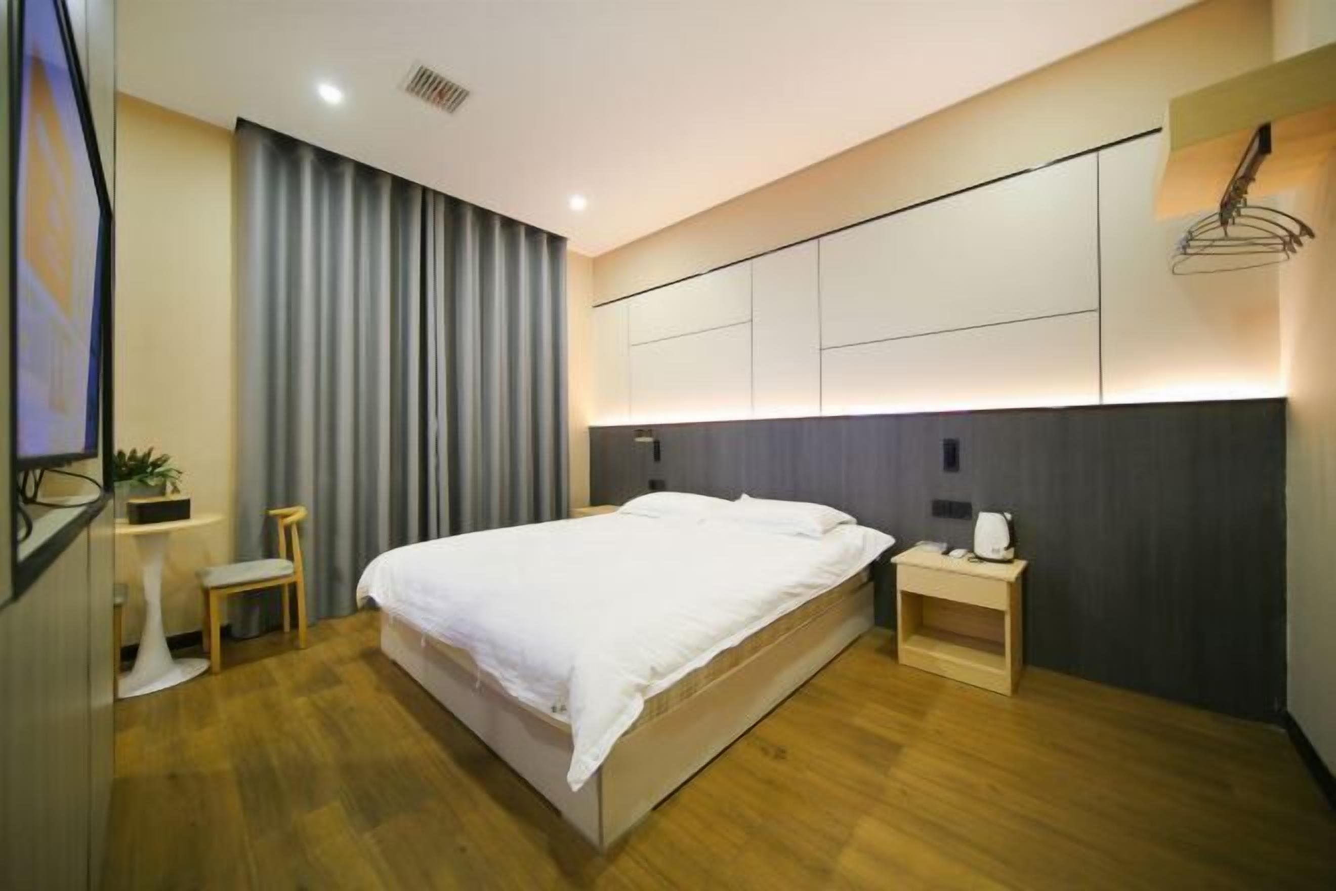 Una habitación de hotel moderna con una cama grande, mesitas de noche, una pequeña zona de estar y un ventanal con cortinas.