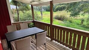 A covered outdoor seating area with a table and chairs, overlooking a garden.