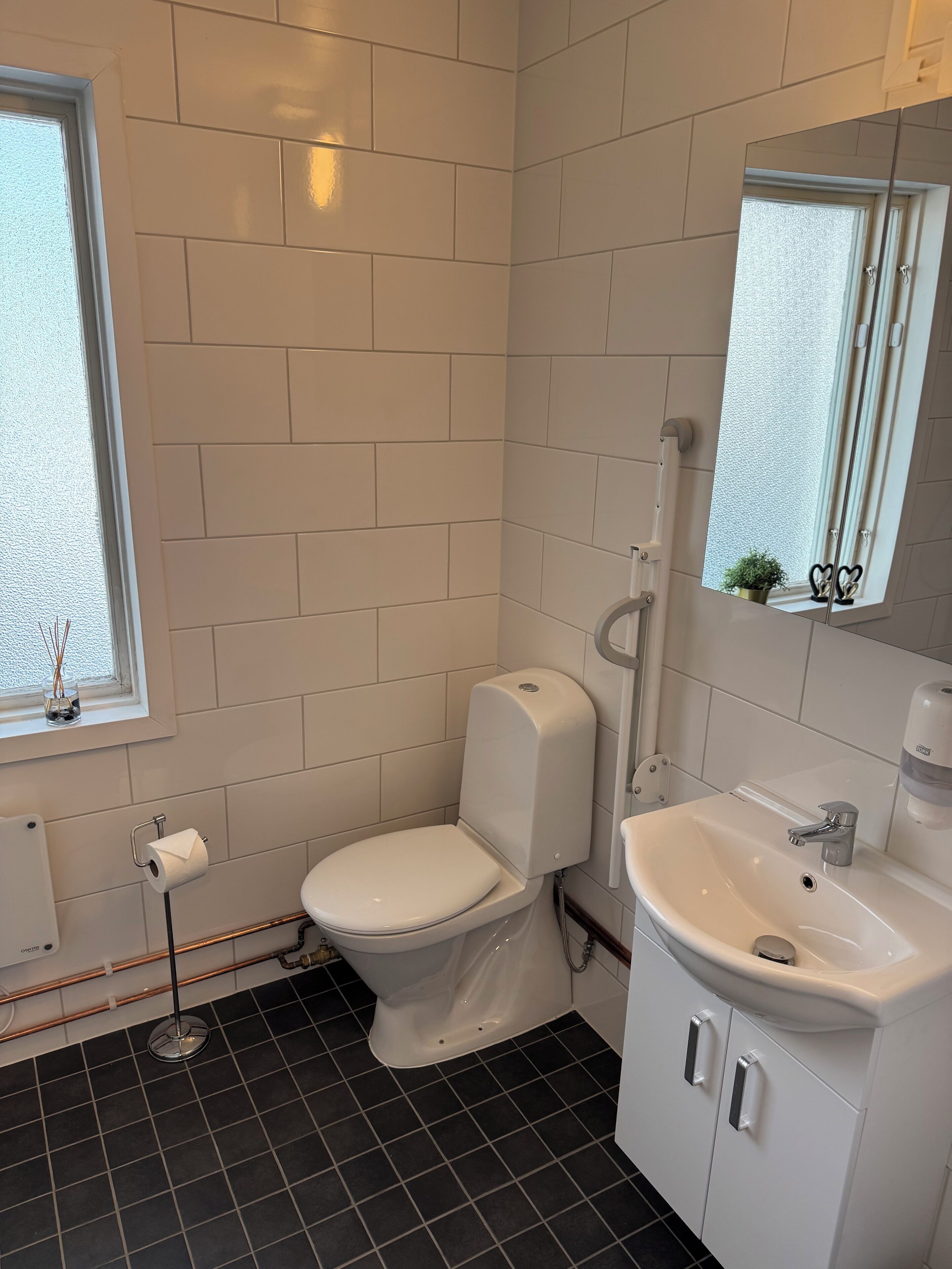 Une salle de bain comprenant des toilettes, un lavabo, un miroir et une fenêtre.
