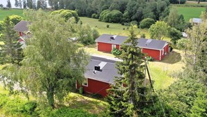 A rural landscape with three red buildings, surrounded by lush greenery and a lake in the background.