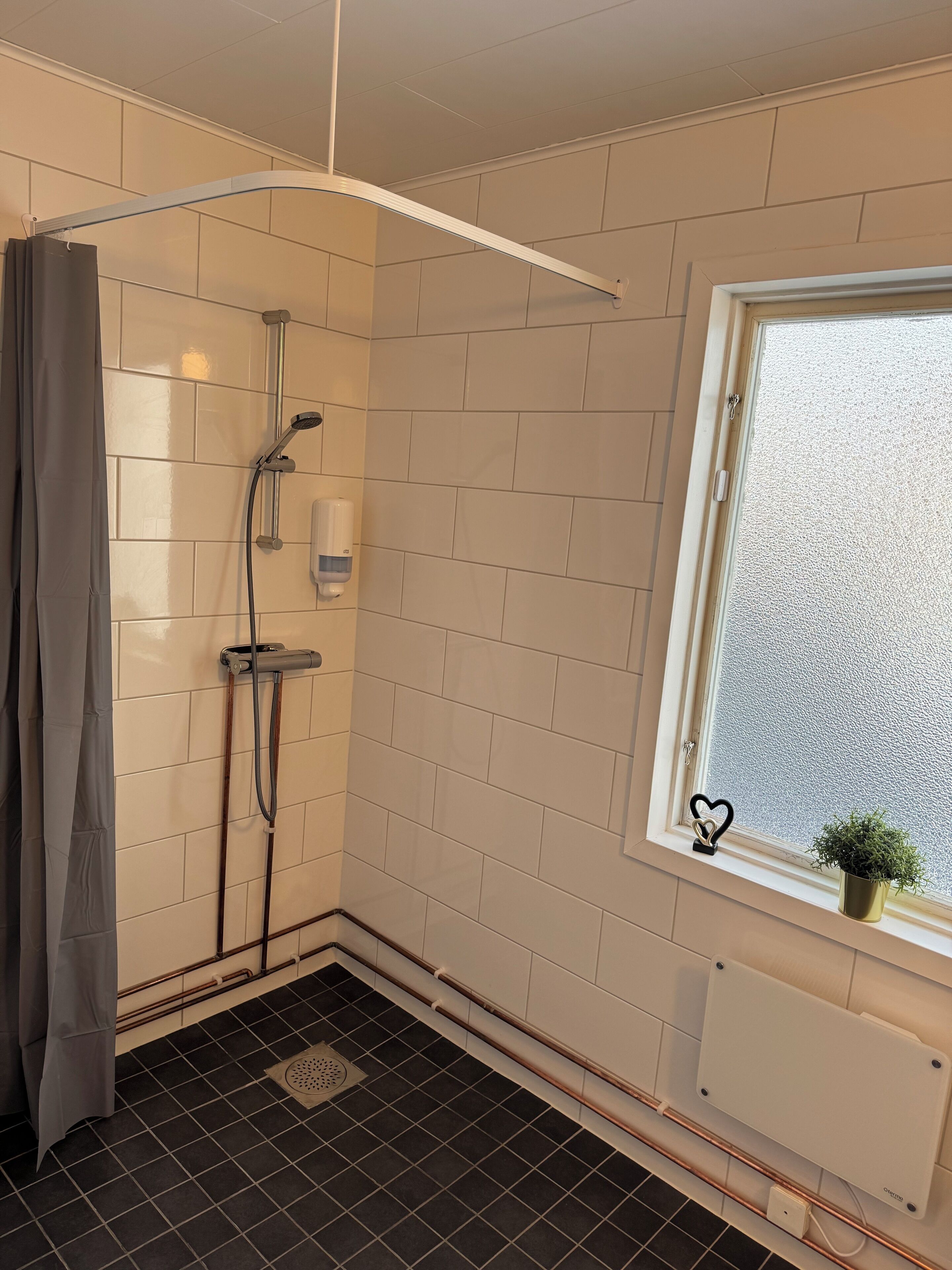 A small bathroom with a shower, a window with a view, and a radiator.