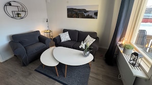A modern living room with two sofas, a white coffee table, a small side table with a lamp, and a large window with curtains.