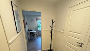 A narrow hallway with wooden flooring, a coat rack, a door, and a framed picture on the wall.
