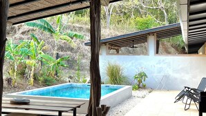 An outdoor pool area with a covered seating area, a wooden table, and a view of a hillside. - CASA ULYSSE 
 2-bedroom house near Tamarindo with swimming pool in the nature (Tamarindo)