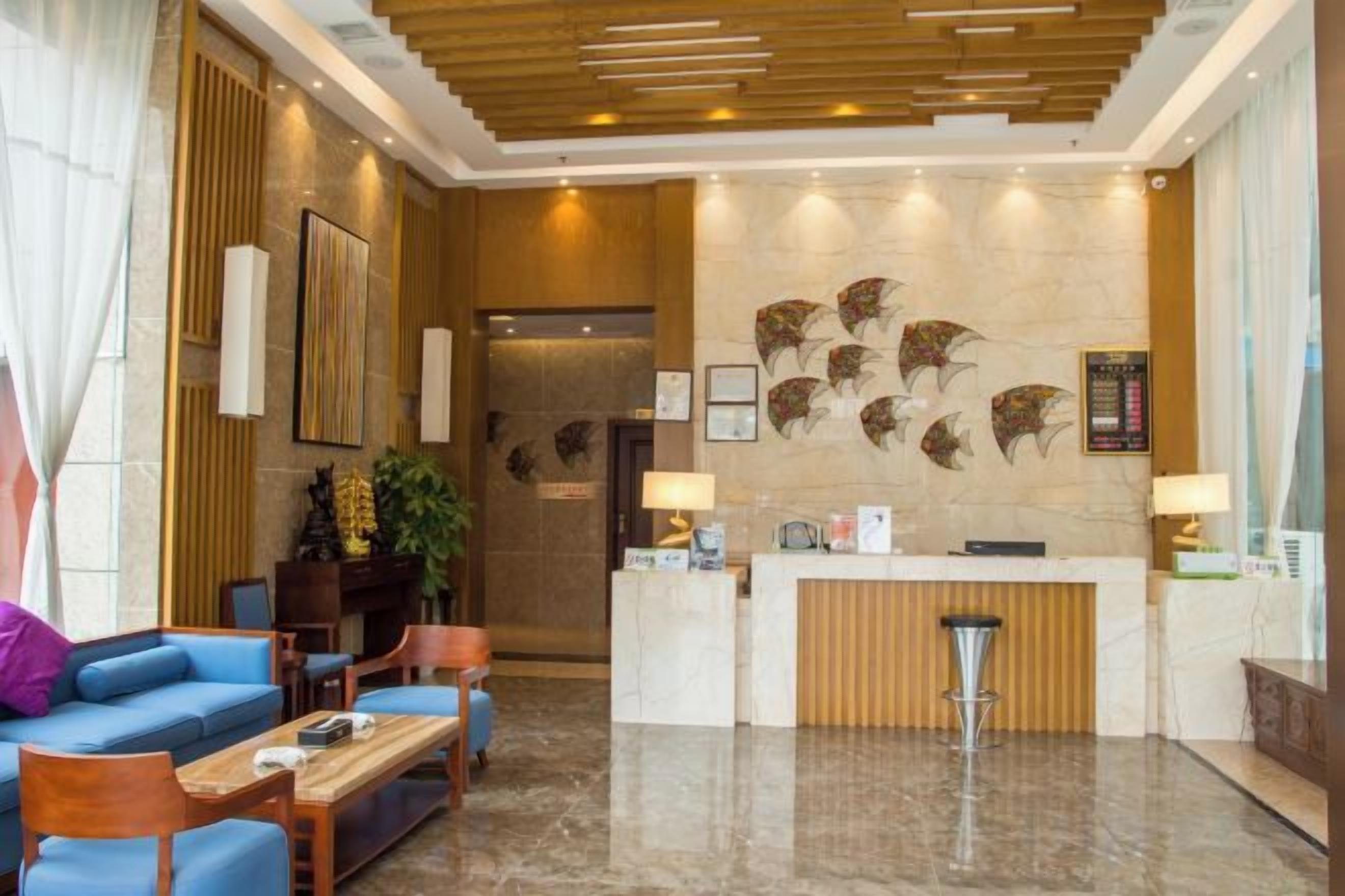 A hotel lobby with a reception desk, seating area, and a wall with decorative elements.