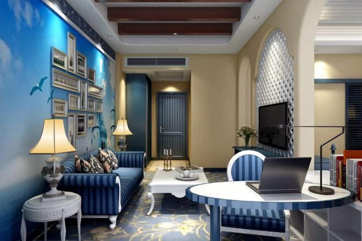 A room with a blue sofa, a round table with a laptop, a white coffee table, and a TV on the wall.
