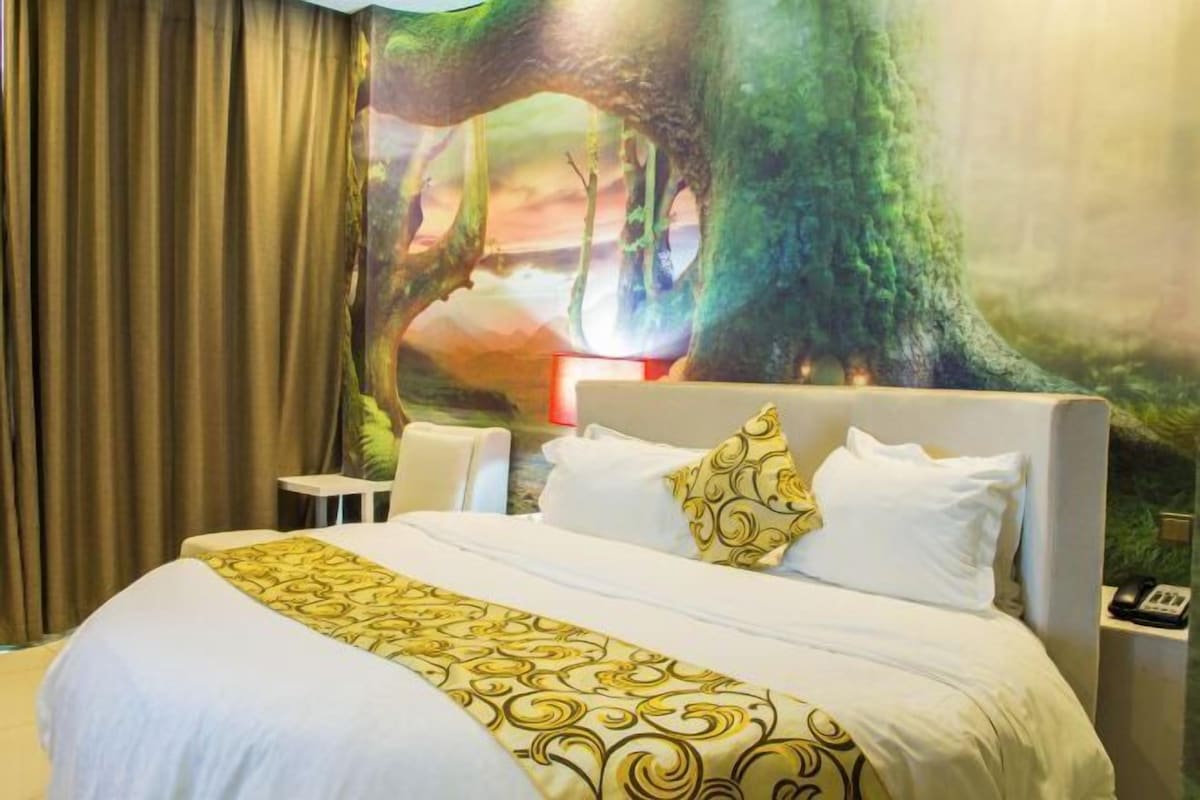 A hotel room with a large bed, white bedding, and a mural of a tree on the wall.