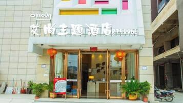 A hotel entrance with a glass door, a signboard, and potted plants.