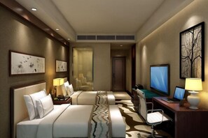 Une chambre d’hôtel avec deux lits, un bureau avec un ordinateur, une télévision et des œuvres d’art accrochées aux murs.