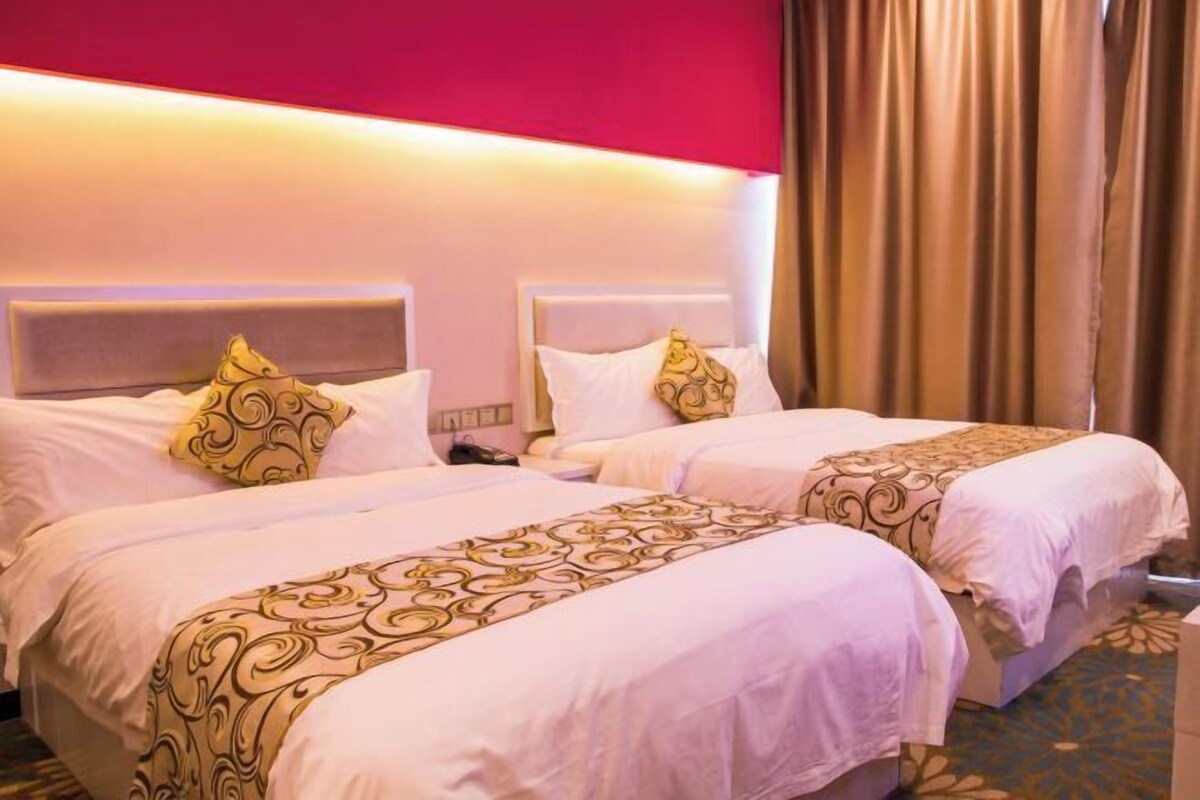 A hotel room with two beds, each with a headboard, a patterned bedspread, and a red accent wall.
