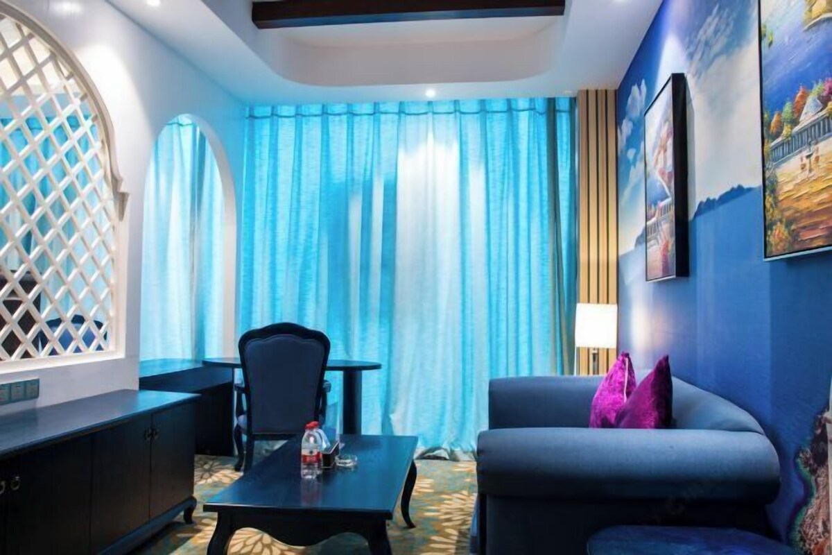 A room with a blue sofa, a small table with a bottle, a chair, and a cabinet.