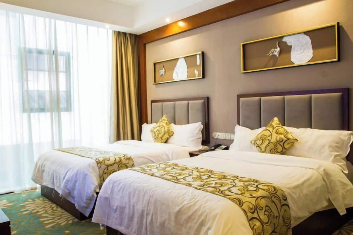 A hotel room with two beds, a large window with curtains, and artwork on the walls.